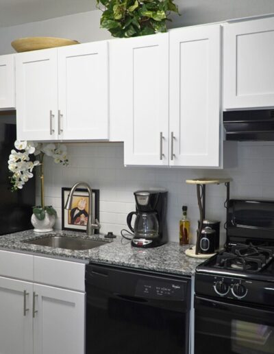 A modern kitchen with white cabinets, subway tile backsplash, granite countertops, and black appliances including a stove and coffee maker. there are decorative plants and an orchid on the counter.