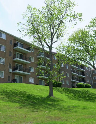 A multi-story brick apartment building in the North Hills set on a lush green hill with young green trees under a clear blue sky.